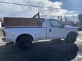 A white 2000 Ford F-350 SD pickup truck with black wheels and a wooden bed cover parked on the side of the road