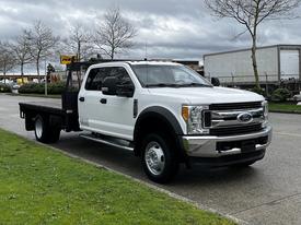 A white 2017 Ford F-550 truck with a flatbed and chrome front grille parked on a street