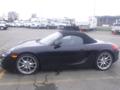 A black 2016 Porsche Boxster with a convertible top and silver alloy wheels parked in a lot