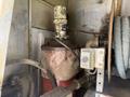 A rusty metallic cylinder with a pipe connected to it sits on a platform with wires and hoses nearby