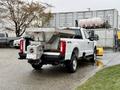 A white 2023 Ford F-250 pickup truck with a large gray bed attachment for hauling and a plow mounted on the front