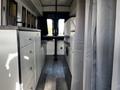 Interior view of a 2017 Ford Transit showing a compact kitchenette with cabinets and a table area alongside seating space