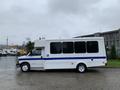 A 2015 Chevrolet Express van with a white body and blue stripe parked on a wet surface showcasing its side profile and large windows