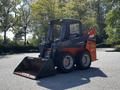 A 2017 Gehl R105 skid steer loader with a black and orange exterior and a front bucket attached sitting on a gravel surface.