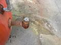 A rusted valve with a hexagon nut connected to a large red air compressor tank