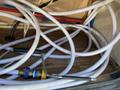 A tangle of white hoses with blue and red lines is coiled inside an enclosed space featuring a valve and a tool attached to one of the hoses