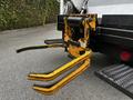 A yellow loading attachment with three pronged forks attached to the back of a 2014 Hino 195 truck