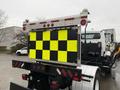 A 2016 Freightliner 108SD truck with a large reflective sign featuring yellow and black checkered patterns mounted on the back