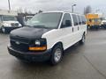 A 2012 Chevrolet Express van with a white body and black hood parked at an angle showcasing its front and side features