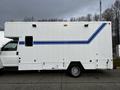 A white 2006 GMC C5000 with a blue stripe on the side and various compartments visible on the lower section of the vehicle