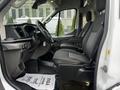 Interior of a 2021 Ford Transit showing the driver's seat and control panel with a spacious cabin design and grey seating upholstery