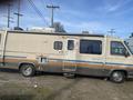 A 1987 Chevrolet Fleetwood Pace Arrow motorhome with a beige and blue striped exterior parked on a dirt surface