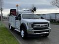 A white 2018 Ford F-550 two-ton truck with a utility body equipped with a crane and a trailer mounted on the back