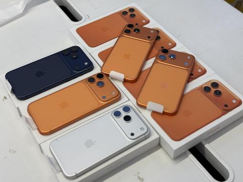Several Apple iPhones in various colors including orange navy and white are arranged on their boxes displaying the Apple logo and camera lenses