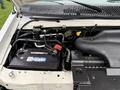 The engine compartment of a 2006 Ford Econoline showing the battery and various engine components with visible labels and hoses