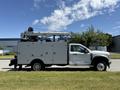 A 2023 Ford F-550 truck with a white body and a raised aerial work platform on top equipped with multiple storage compartments