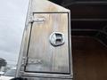 A metallic storage compartment door of a 2011 Dodge Ram 5500 with a round handle and visible wear marks on the surface