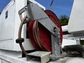A metal hose reel with red hose and connections mounted on a white utility vehicle