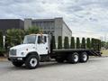 A 1998 Freightliner FL80 flatbed truck with a white cab and black flatbed, featuring dual rear wheels and safety lights on top