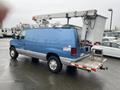 A blue 2006 Ford Econoline van with a raised bucket lift attached to the roof and a rear step platform