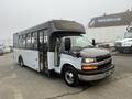 A 2017 Chevrolet Express bus with a white body and gray front is parked with its door open and visible seating inside