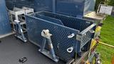 A blue metal truck bed with a metal mesh storage container secured by brackets and hooks on a textured surface