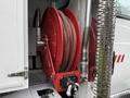 A red hose reel mounted on a white vehicle with a black hose coiled around it and a nozzle attached at the bottom