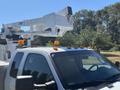 A white 2016 Ford F-550 with an elevated lift mechanism mounted on the truck bed and amber lights on the roof