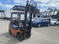 A 2010 Toyota 7FGGU25 forklift with a red and black exterior featuring a raised fork and a seating area for the operator