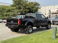 A black 2021 Ford F-350 Super Duty pickup truck with a crew cab and large tires is parked, showcasing its robust design and rear-end features