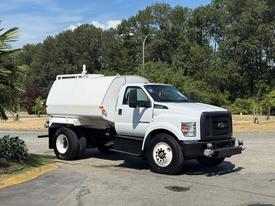 A 2019 Ford F-750 truck in white with a large tank in the bed is parked, facing the camera with visible details like the grille and wheels