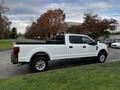 A white 2020 Ford F-250 Super Duty truck parked on a street with a flatbed and chrome wheels