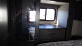 A dark wooden cabinet with a mirrored door and a small drawer sits beside a bed in a recreational vehicle interior