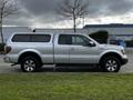 A silver 2014 Ford F-150 with a matching cap on the truck bed parked on grass with a side view