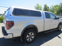 A silver 2014 Ford F-150 pickup truck with a camper shell on the bed and alloy wheels parked on a surface