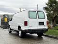 A white 2006 Ford Econoline van parked with its rear facing towards the viewer showing windows and a blank license plate area