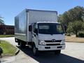 A 2018 Hino 195 truck with a white body and a large cargo box is parked with the front facing the viewer