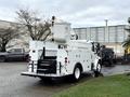 A white 2005 Freightliner M2 106 bucket truck with an elevated work platform and storage compartments in the rear