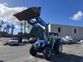A blue 2010 New Holland T4050 tractor with a raised front loader and large tires is positioned at a construction site