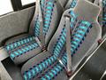 Two gray bus seats with blue and black stripes, featuring seatbelts, are positioned next to each other in a bus interior