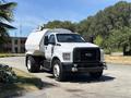 A 2019 Ford F-750 truck with a white cab and a large tank mounted in the truck bed positioned on a paved road