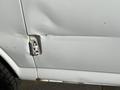 A close-up of a dented white 2012 GMC Savana van door with visible rust around the hinge area