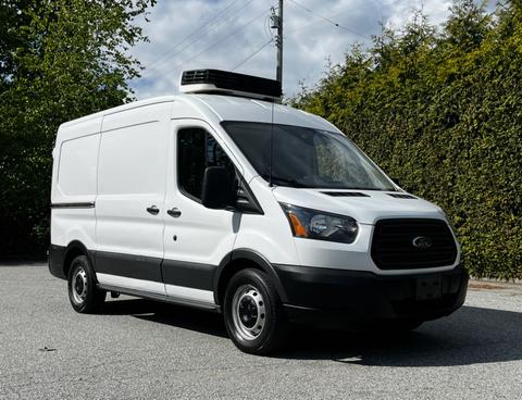 A white 2015 Ford Transit van with a black roof mounted air conditioning unit parked at an angle
