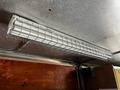 A metal fluorescent light fixture with a protective wire guard mounted on a ceiling interior