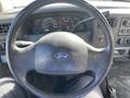 A black steering wheel with a Ford logo at the center is prominently displayed in the foreground with instrument gauges visible behind it