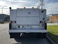 White 2018 Ford F-550 with a ladder rack and utility body featuring multiple lights and reflectors at the rear