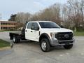 A white 2020 Ford F-550 pickup truck with a flatbed body and dual rear wheels is parked at an angle