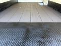 A 2013 Isuzu NPR truck with a flatbed surface featuring a smooth wooden floor and a textured black metal loading area