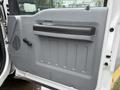 The interior door panel of a 2012 Ford F-450 SD featuring a textured gray surface a black handle and a manual window crank