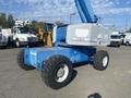 A blue 1997 Genie S-65 4X4 articulated boom lift with large rubber tires and a raised platform for elevated work